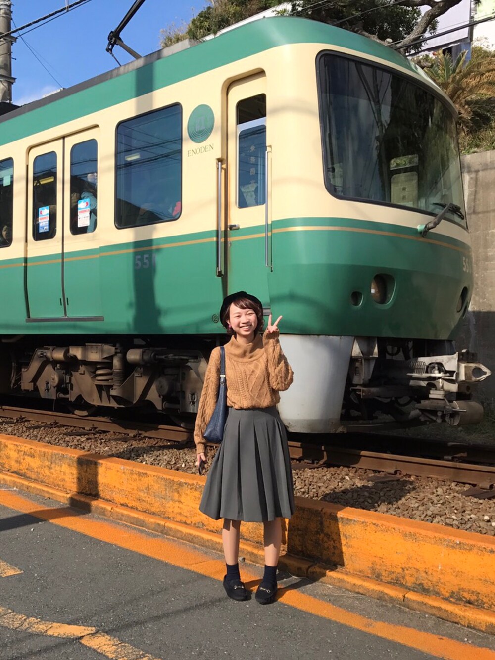 ブラウン系のニット/セーター、グリーン系のスカート、ブルー系のショルダーバッグを着用したレディースの秋コーディネートの1枚目の写真