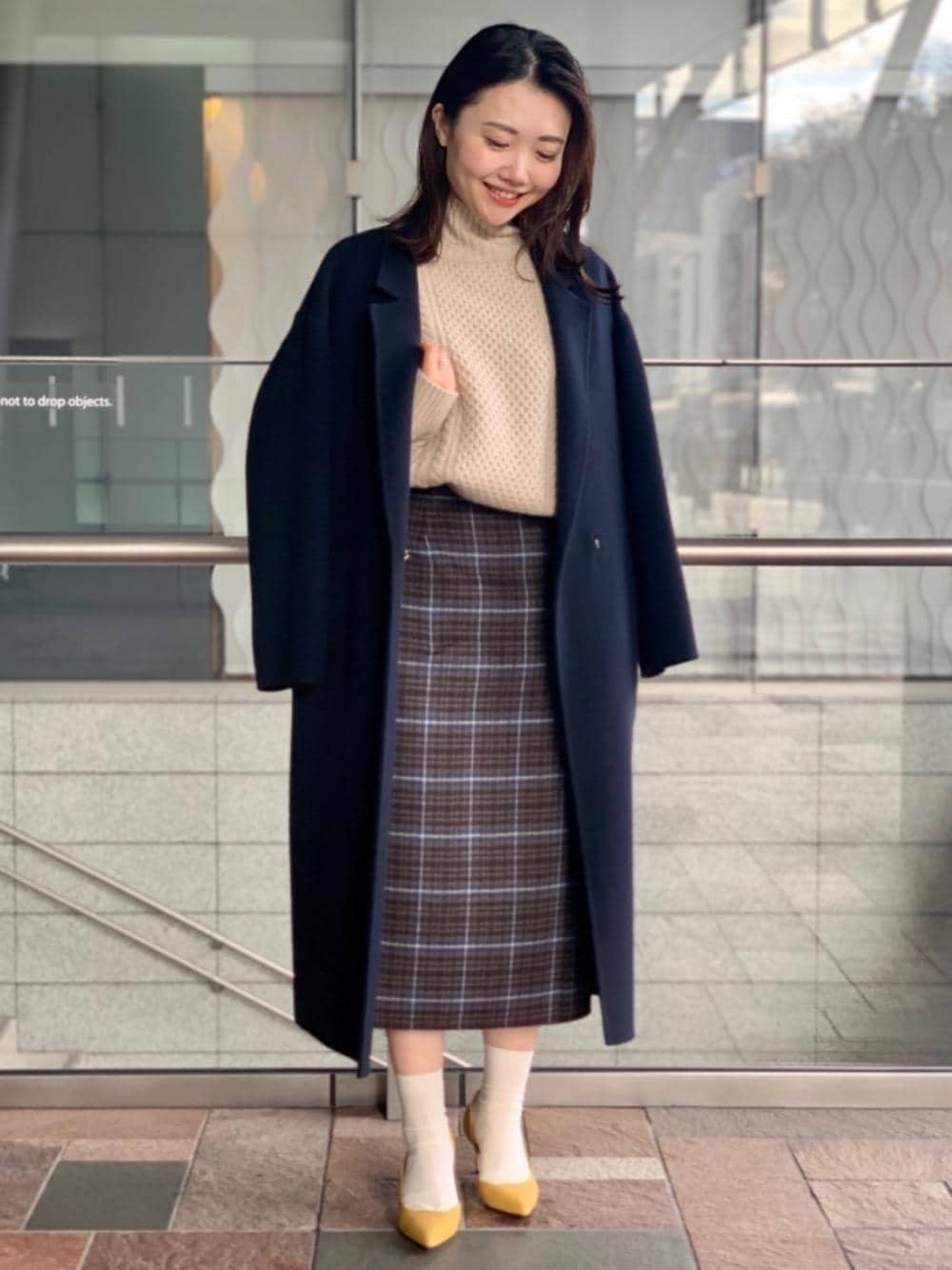 イエロー系のパンプス、ベージュ系のニット/セーター、ブルー系のチェスターコートを着用したレディースの冬コーディネートの1枚目の写真