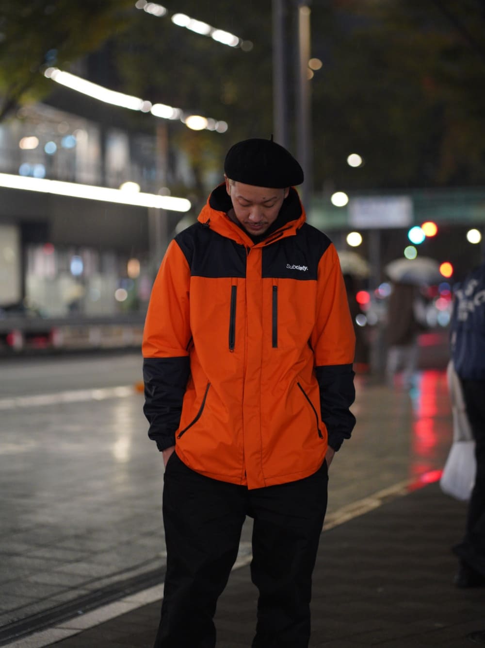 オレンジ系のマウンテンパーカー、ブラック系のハンチング/ベレー帽を着用したメンズの秋コーディネートの1枚目の写真