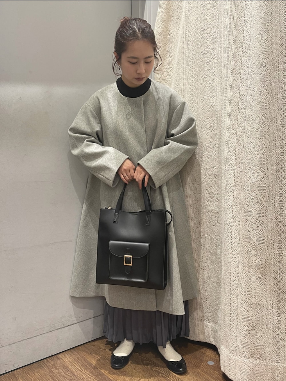 グレー系のノーカラーコート、ブルー系のスカート、ブラック系のトートバッグを着用したレディースの冬コーディネートの1枚目の写真