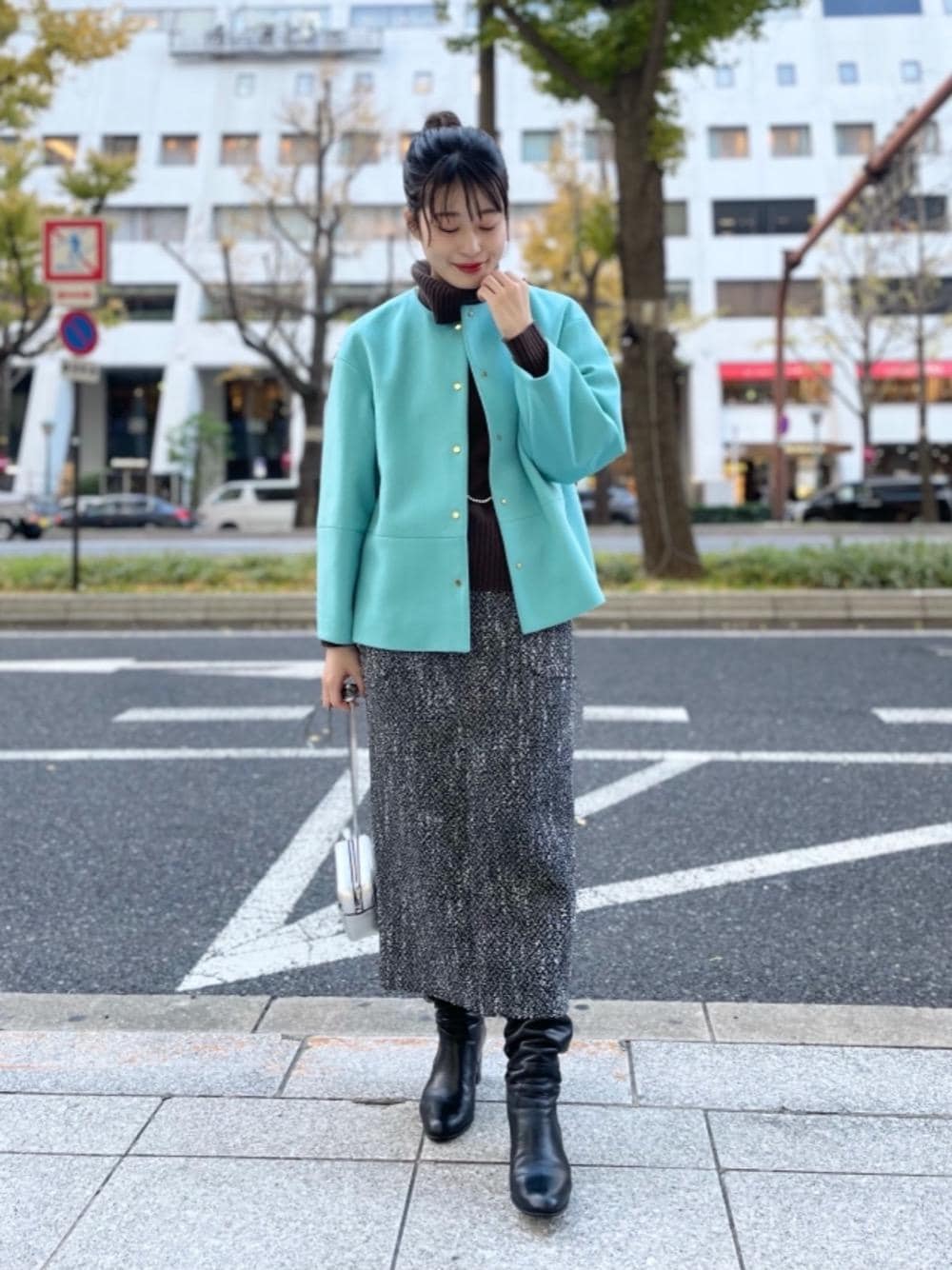 グリーン系のノーカラーコート、ブラウン系のニット/セーター、ブラック系のスカートを着用したレディースの冬コーディネートの1枚目の写真
