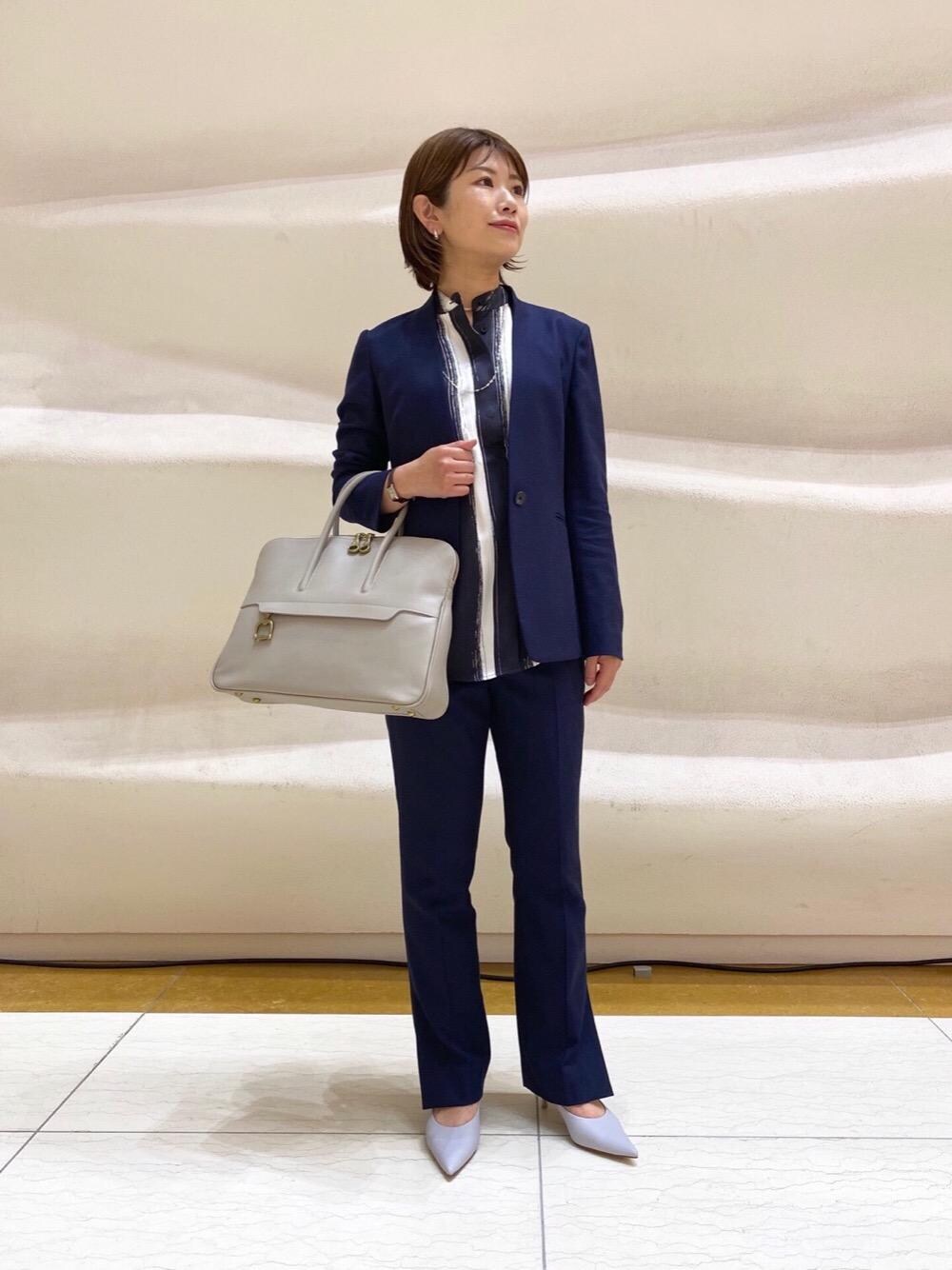 グレー系のビジネスバッグ、ブルー系のノーカラージャケット、ブルー系のスラックスを着用したレディースの春コーディネートの1枚目の写真