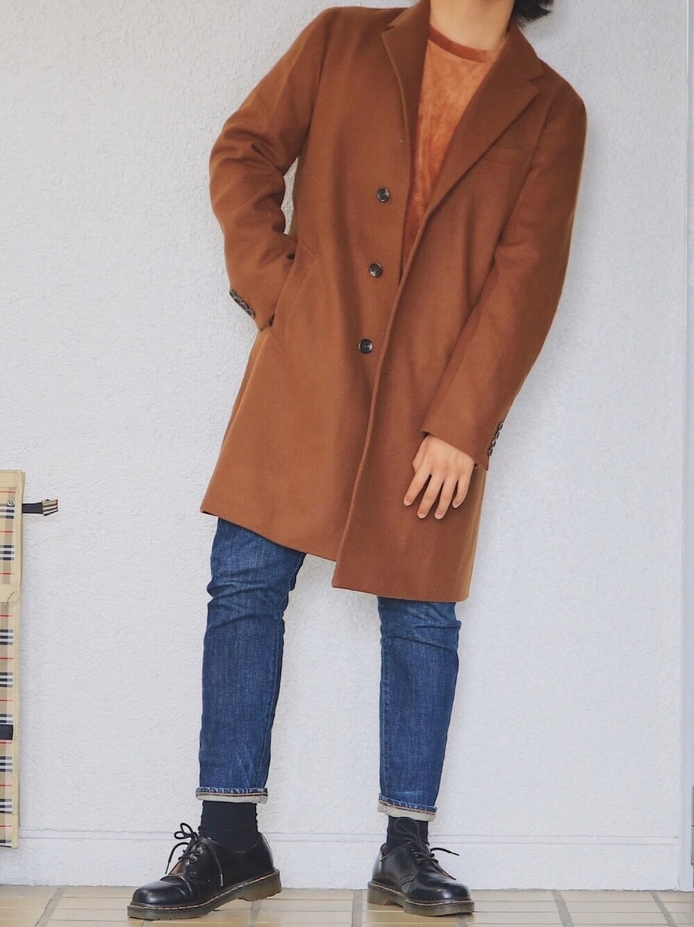 ブラウン系のチェスターコート、ブルー系のデニムパンツ、ブラウン系のTシャツ/カットソーを着用したメンズの秋コーディネートの1枚目の写真