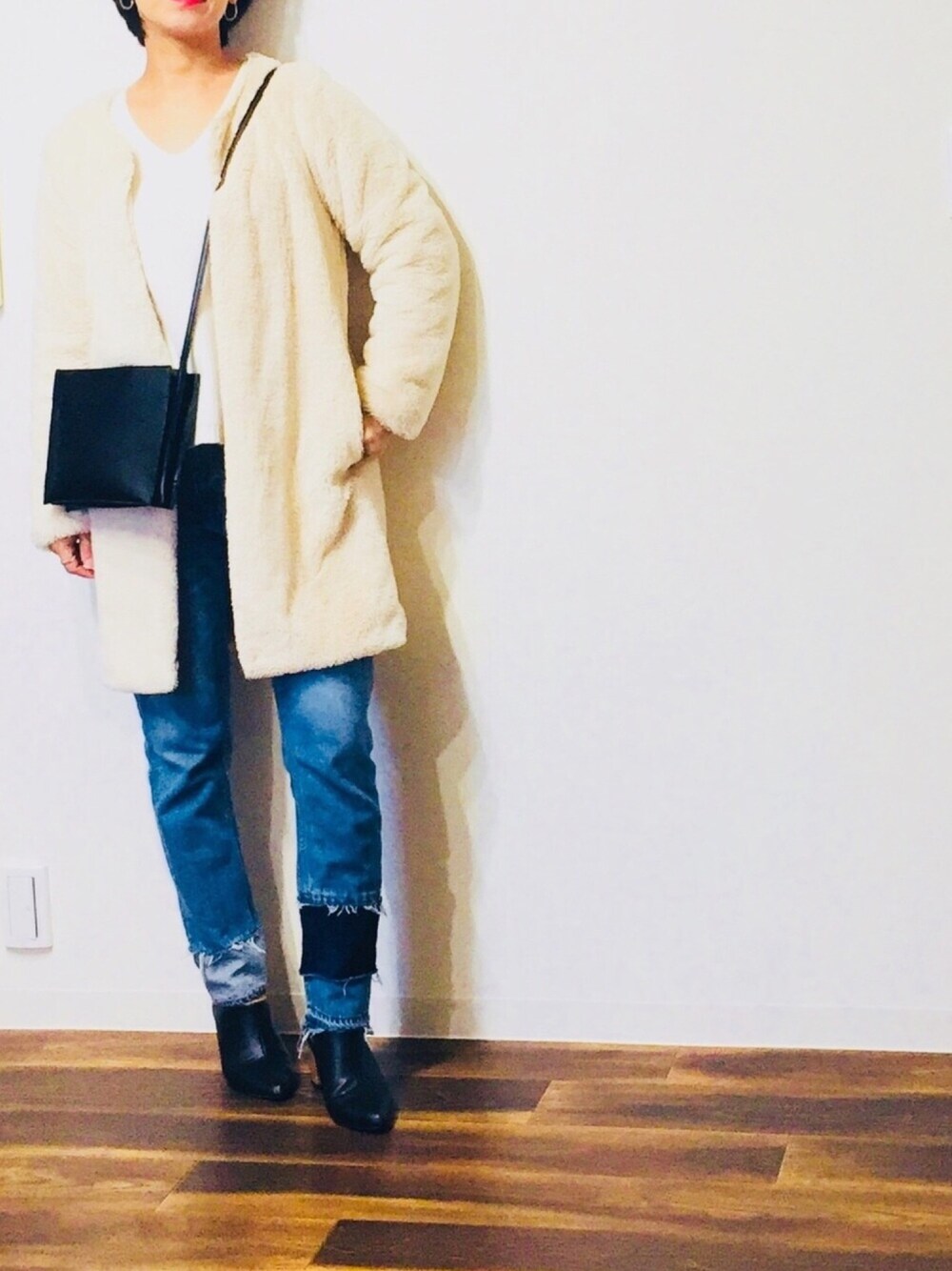 ブラック系のショルダーバッグ、ブルー系のデニムパンツ、ホワイト系のムートンコートを着用したレディースの秋コーディネートの1枚目の写真