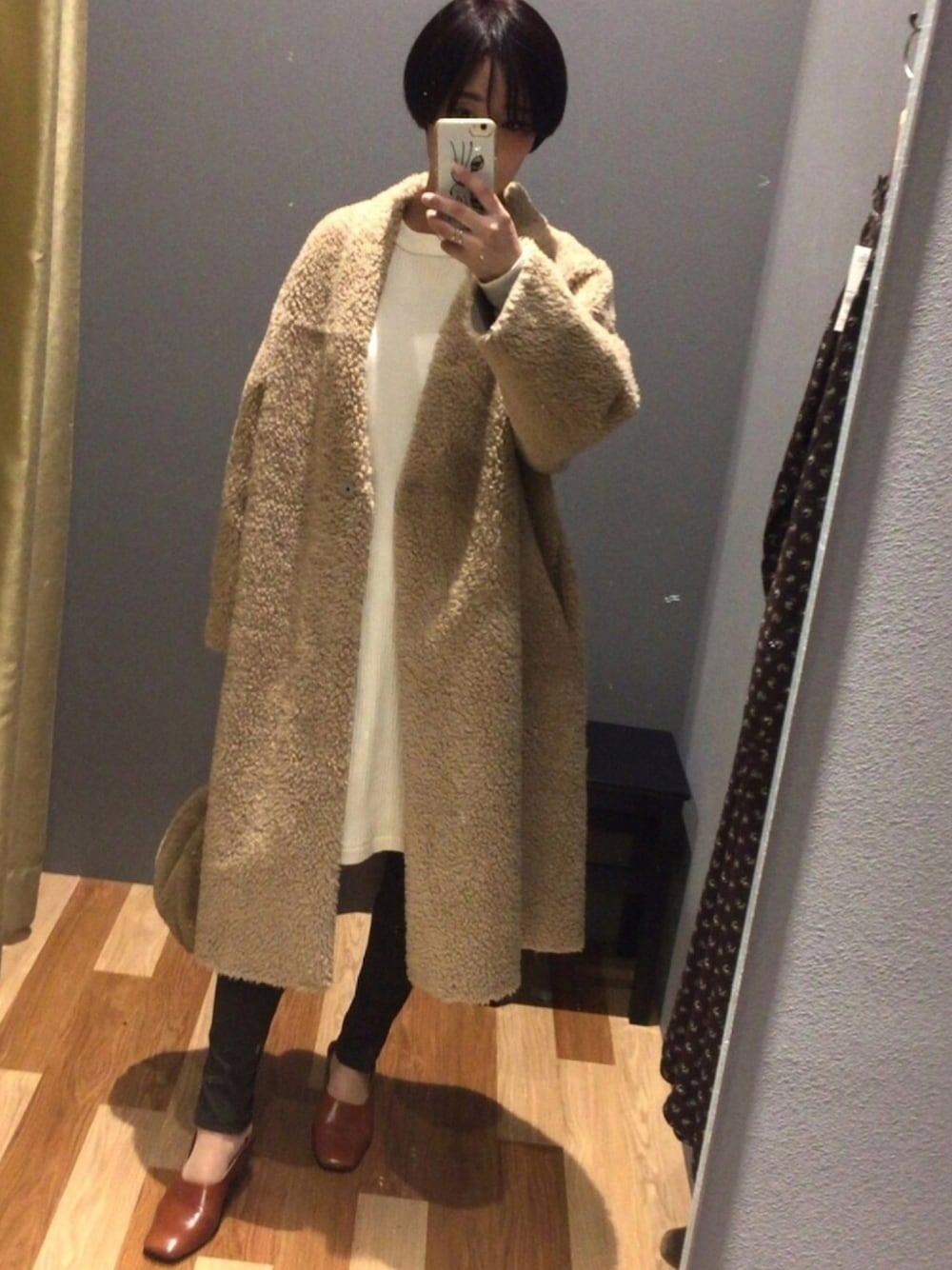 ベージュ系のステンカラーコート、ホワイト系のワンピース、ブラウン系のパンプスを着用したレディースの冬コーディネートの1枚目の写真