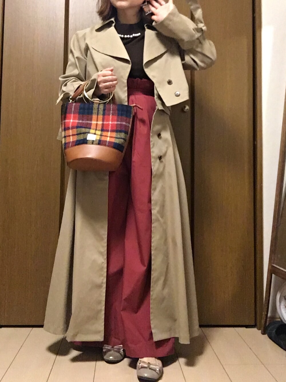 ブラウン系のニット/セーター、レッド系のその他パンツ、ベージュ系のトレンチコートを着用したレディースの冬コーディネートの1枚目の写真