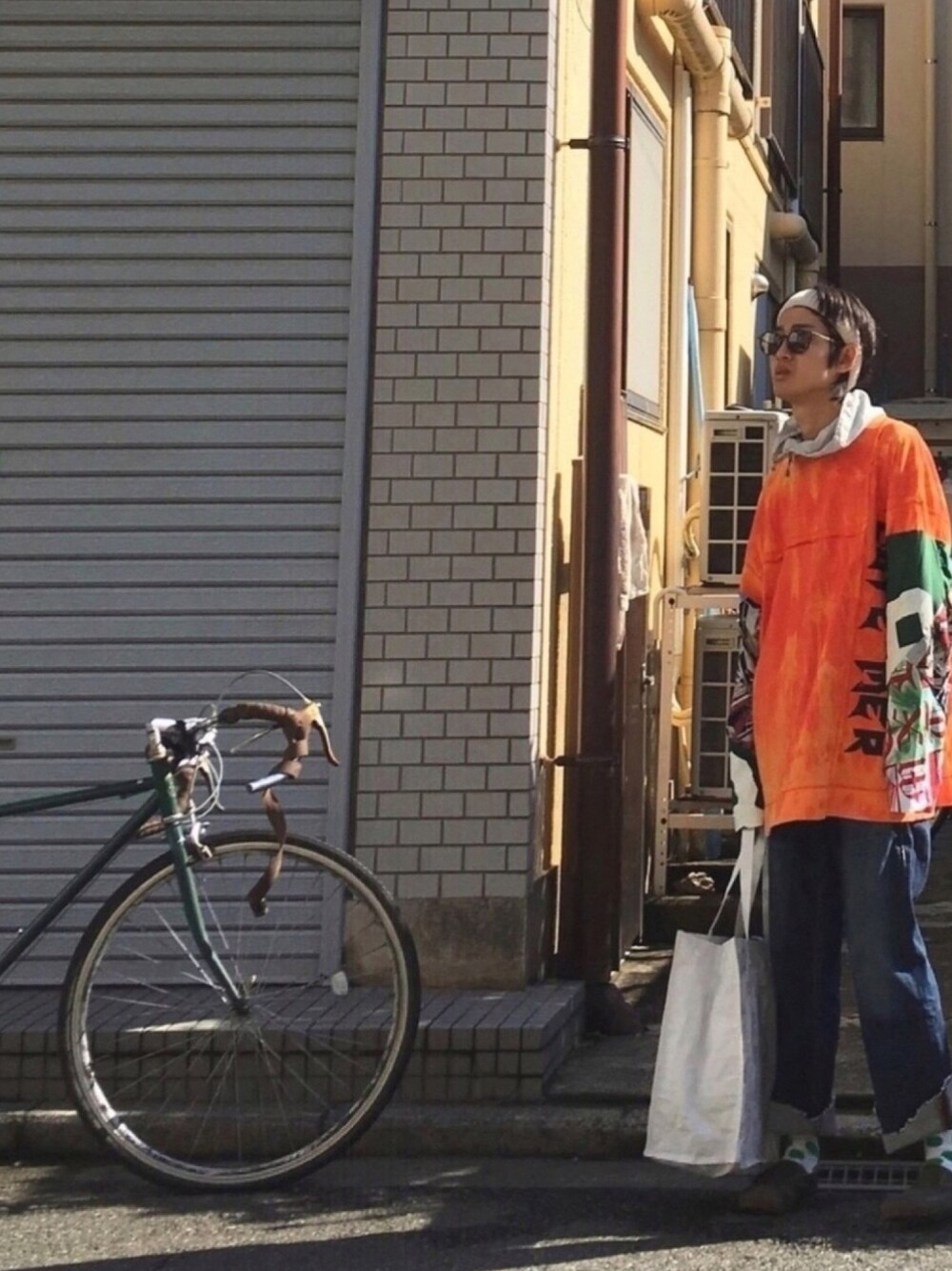 オレンジ系のTシャツ/カットソー、シルバー系のその他アウター、ブルー系のデニムパンツを着用したメンズの秋コーディネートの1枚目の写真