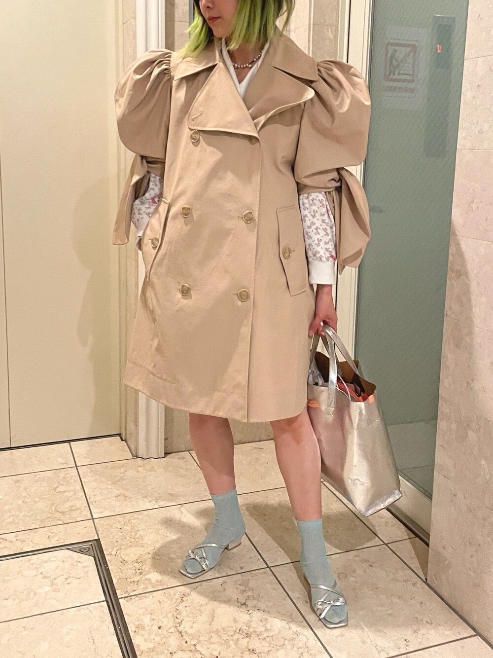 ベージュ系のトレンチコート、ホワイト系のトップス、シルバー系のサンダルを着用したレディースの春コーディネートの1枚目の写真