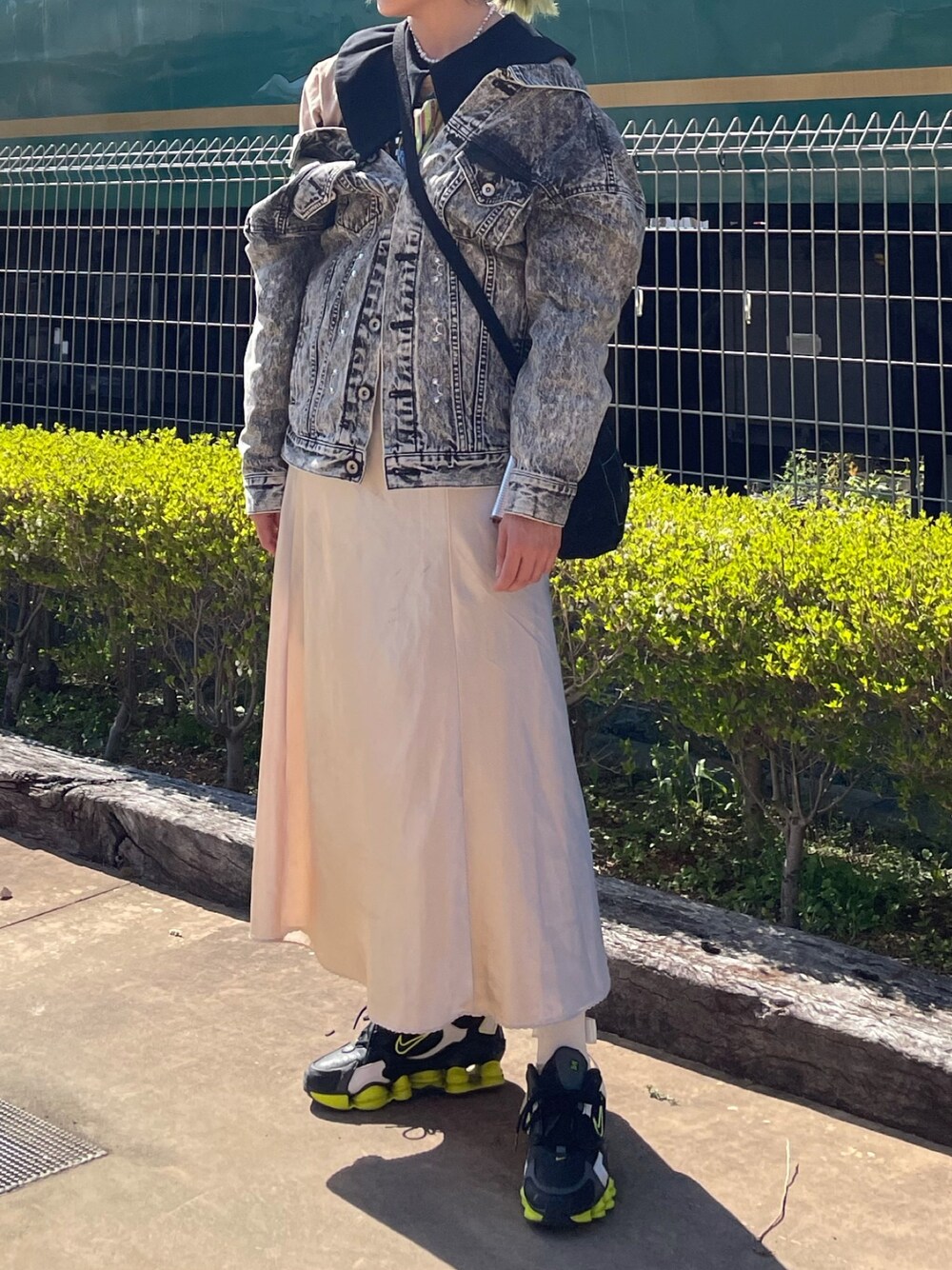 ブラック系のデニムジャケット、ベージュ系のスカート、ブラック系のスニーカーを着用したレディースの春コーディネートの1枚目の写真