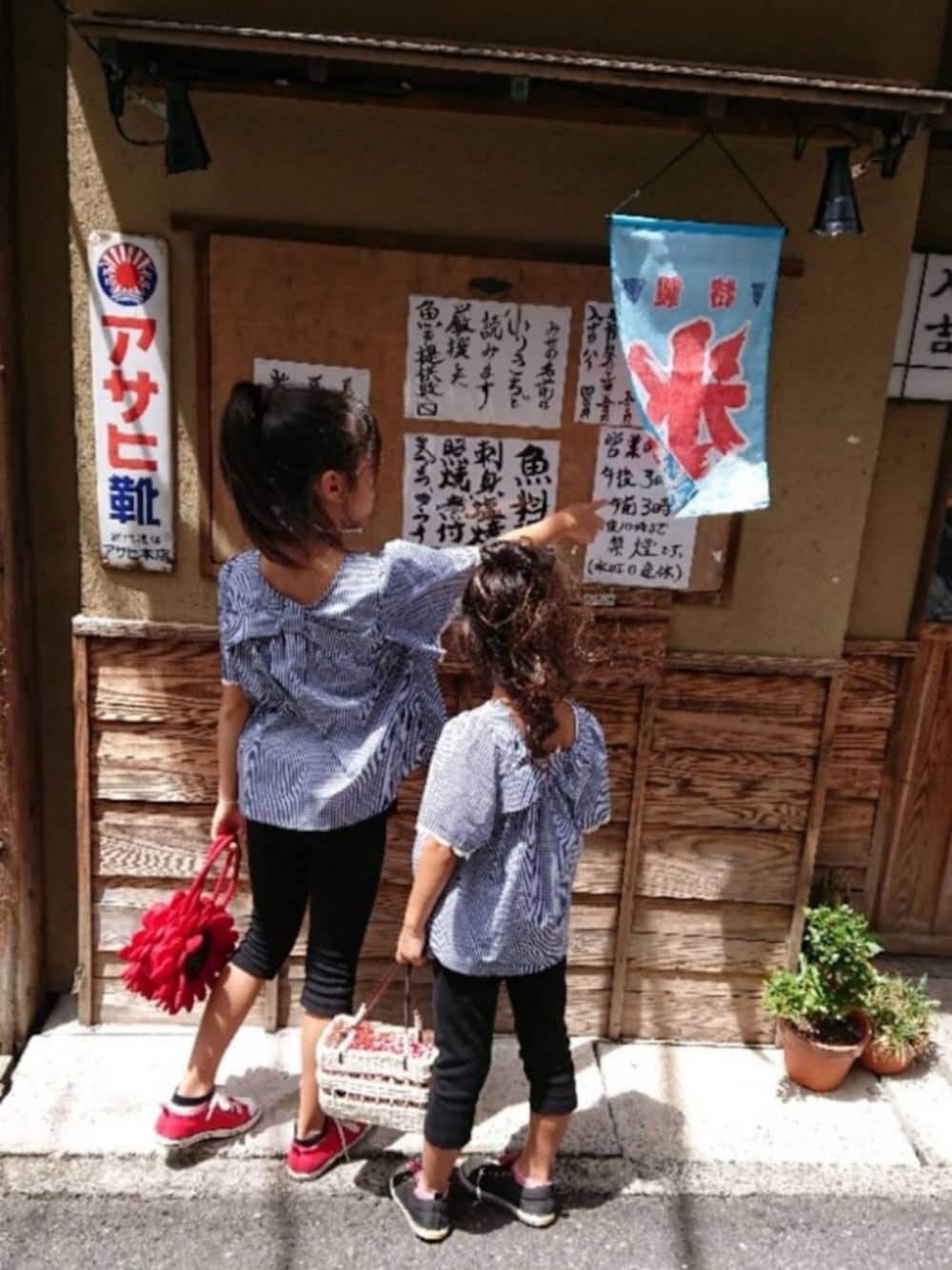 レッド系のかごバッグ、ブラック系のスニーカー、ブラック系のトップスを着用したキッズの夏コーディネートの1枚目の写真