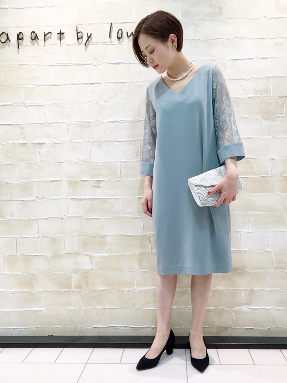 グリーン系のドレス、ホワイト系のクラッチバッグ、ブラック系のパンプスを着用したレディースの春コーディネートの1枚目の写真