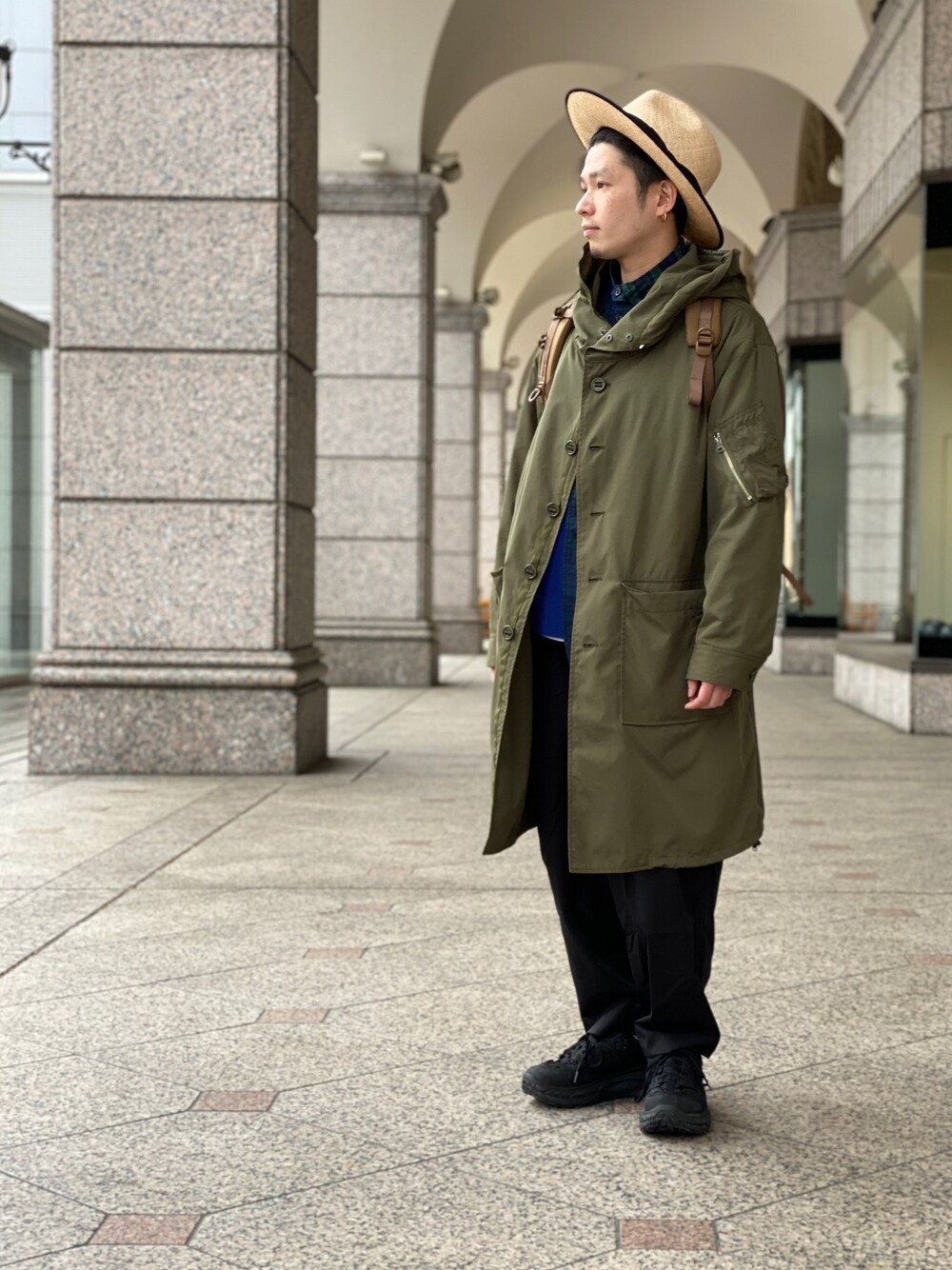 グリーン系のステンカラーコート、ブラック系のその他パンツ、ブラック系のスニーカーを着用したメンズの春コーディネートの1枚目の写真