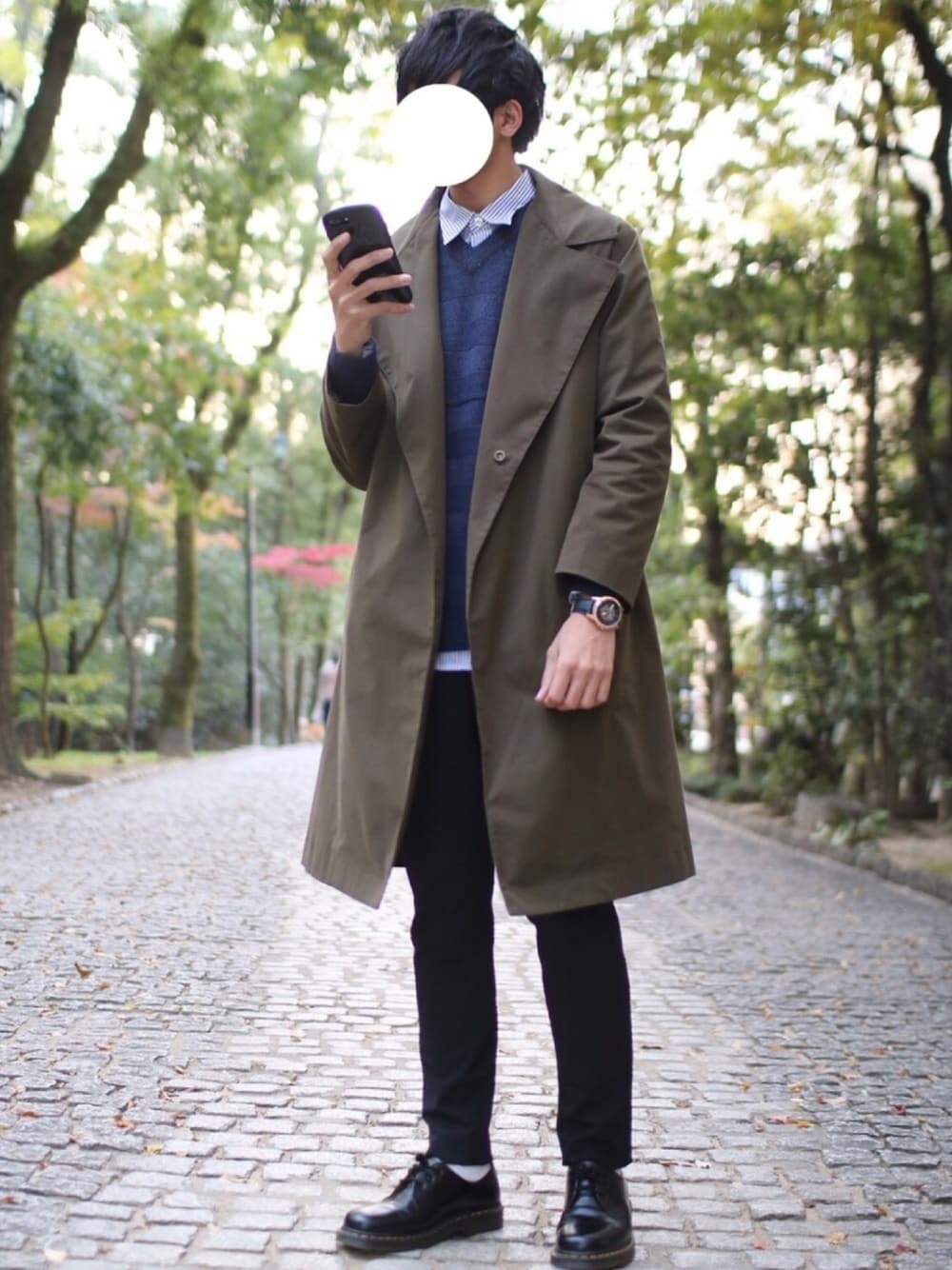 グリーン系のステンカラーコート、ブルー系のニット/セーター、ブラック系のスラックスを着用したメンズの秋コーディネートの1枚目の写真