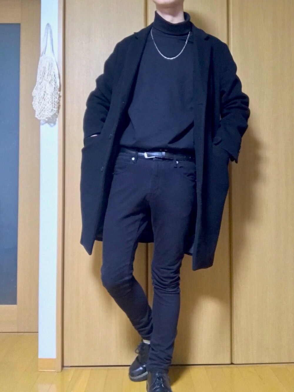 ブラック系のデニムパンツ、ホワイト系のTシャツ/カットソー、ブラック系のチェスターコートを着用したメンズの冬コーディネートの1枚目の写真