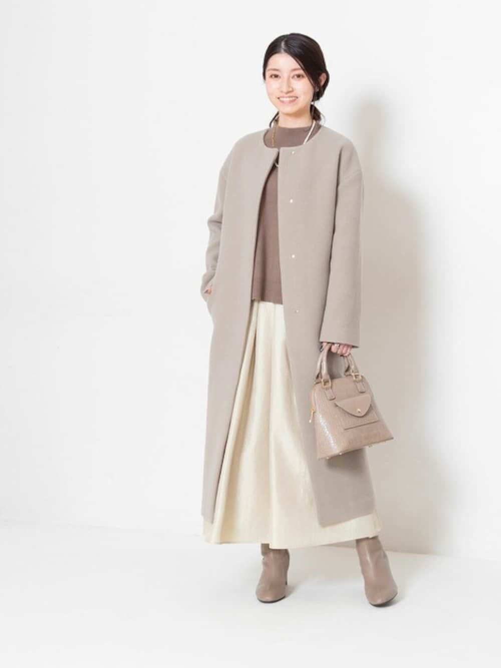 グリーン系のノーカラーコート、ブラウン系のニット/セーター、イエロー系のスカートを着用したレディースの冬コーディネートの1枚目の写真