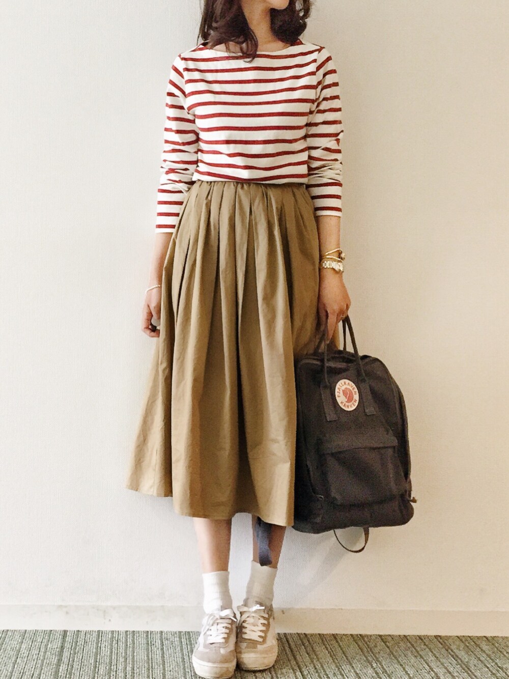 レッド系のTシャツ/カットソー、ベージュ系のスカート、グレー系のバックパック/リュックを着用したレディースの春コーディネートの1枚目の写真