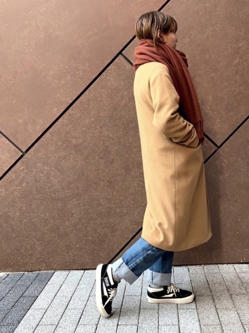 イエロー系のピーコート、ブルー系のデニムパンツ、ブラック系のスニーカーを着用したレディースの冬コーディネートの1枚目の写真