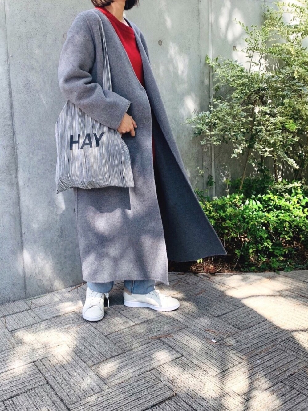 グレー系のノーカラーコート、レッド系のニット/セーター、ブルー系のデニムパンツを着用したレディースの秋コーディネートの1枚目の写真