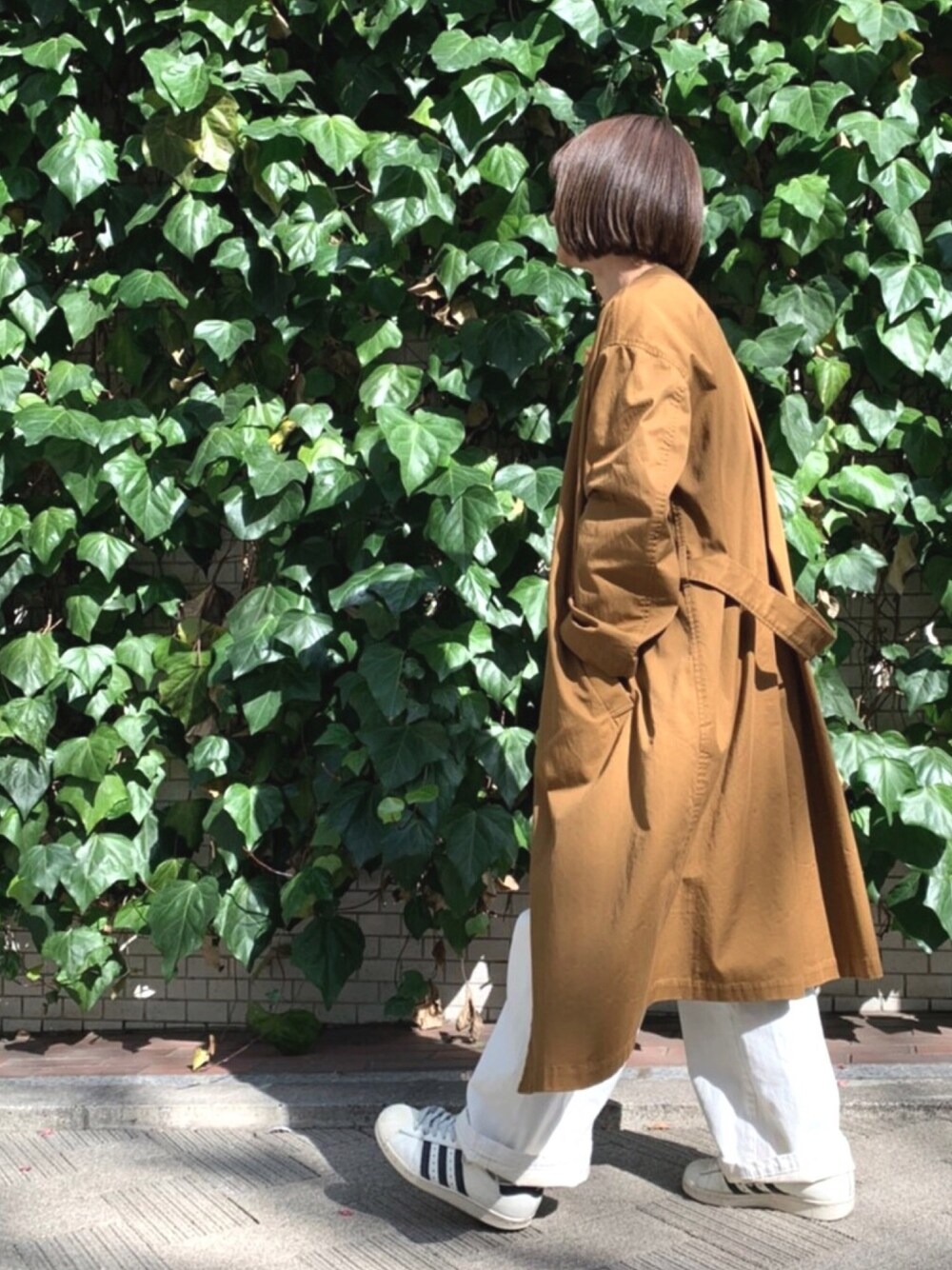 ブラウン系のノーカラーコート、ホワイト系のサロペット/オーバーオール、ホワイト系のスニーカーを着用したレディースの冬コーディネートの1枚目の写真