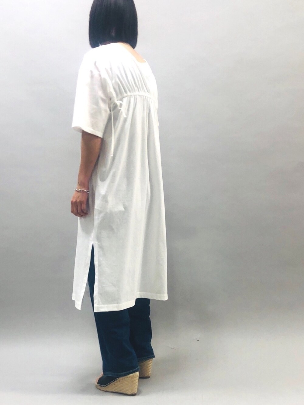 ホワイト系のワンピース、ブルー系のデニムパンツ、ブラック系のサンダルを着用したレディースの夏コーディネートの1枚目の写真