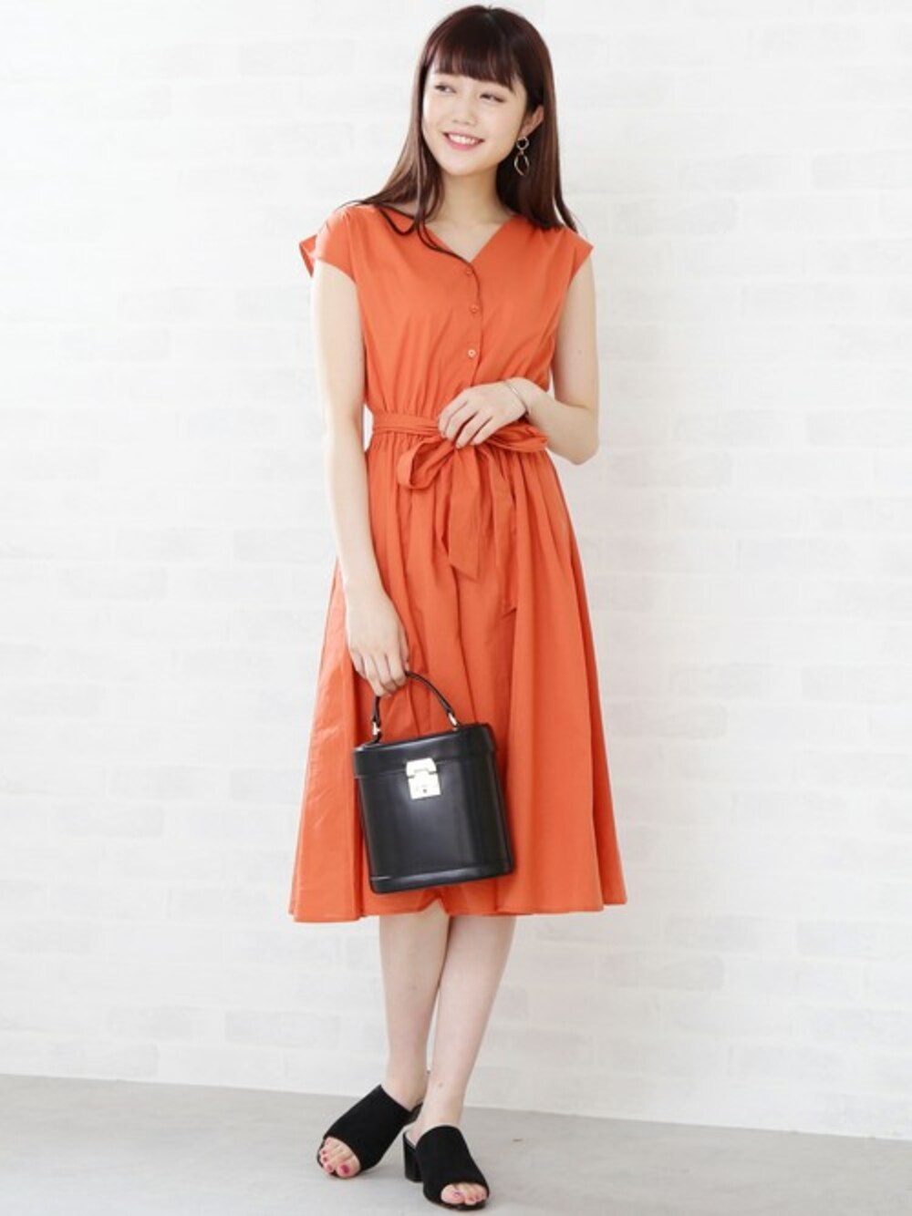 オレンジ系のワンピース、ブラック系のトートバッグ、ゴールド系のバングル/リストバンドを着用したレディースの春コーディネートの1枚目の写真