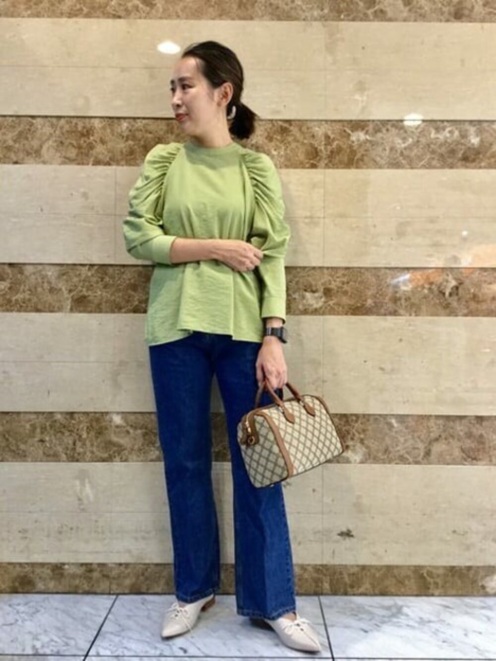グリーン系のシャツ/ブラウス、ベージュ系のボストンバッグ、ブルー系のデニムパンツを着用したレディースの秋コーディネートの1枚目の写真