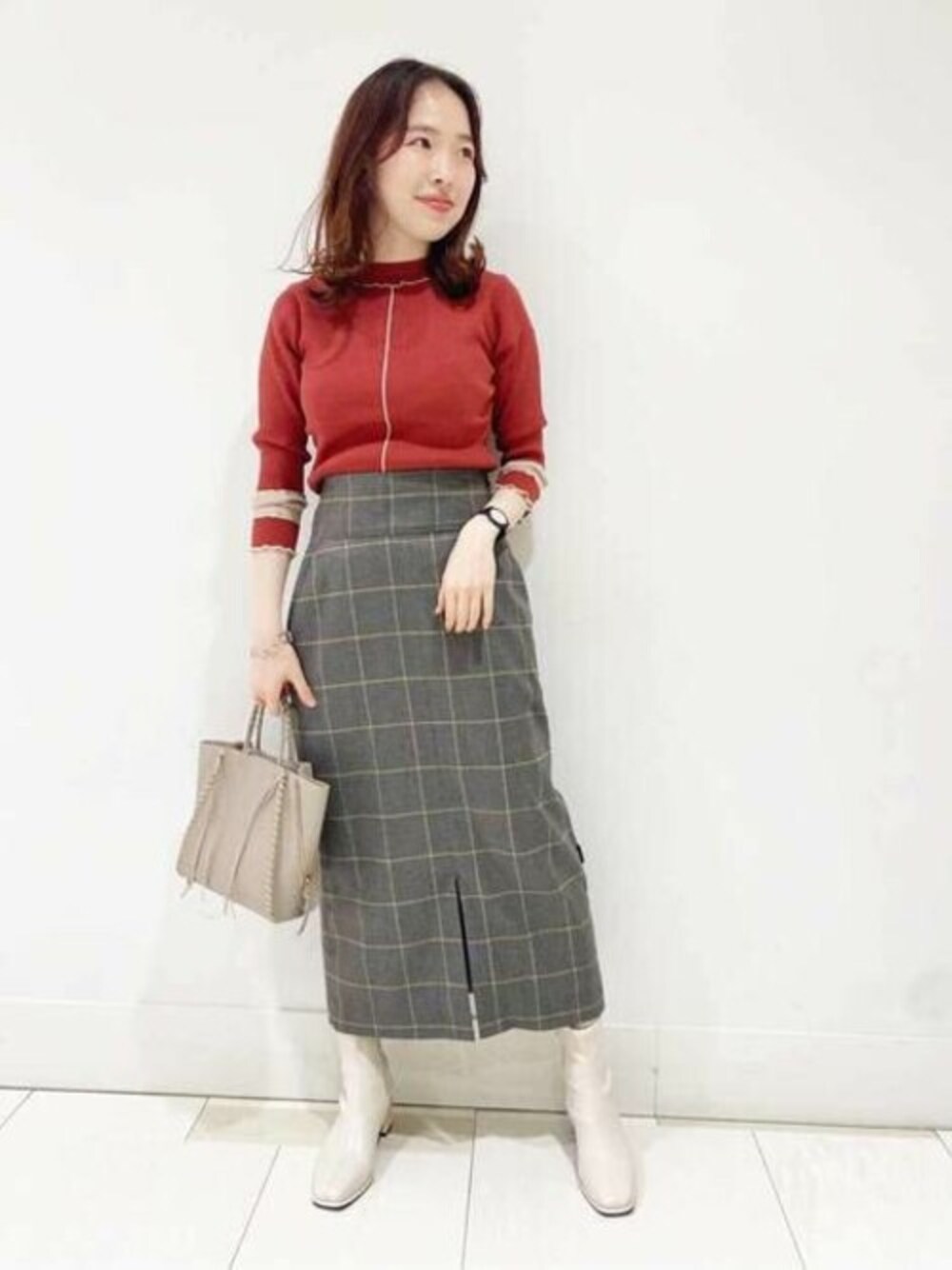 レッド系のニット/セーター、グレー系のスカート、ホワイト系のブーツを着用したレディースの秋コーディネートの1枚目の写真