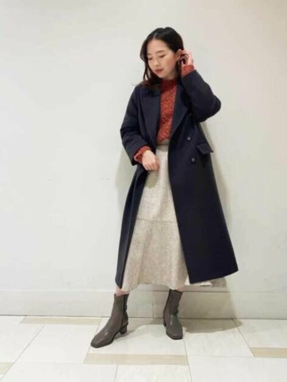 レッド系のニット/セーター、ベージュ系のスカート、ブラウン系のブーツを着用したレディースの冬コーディネートの1枚目の写真