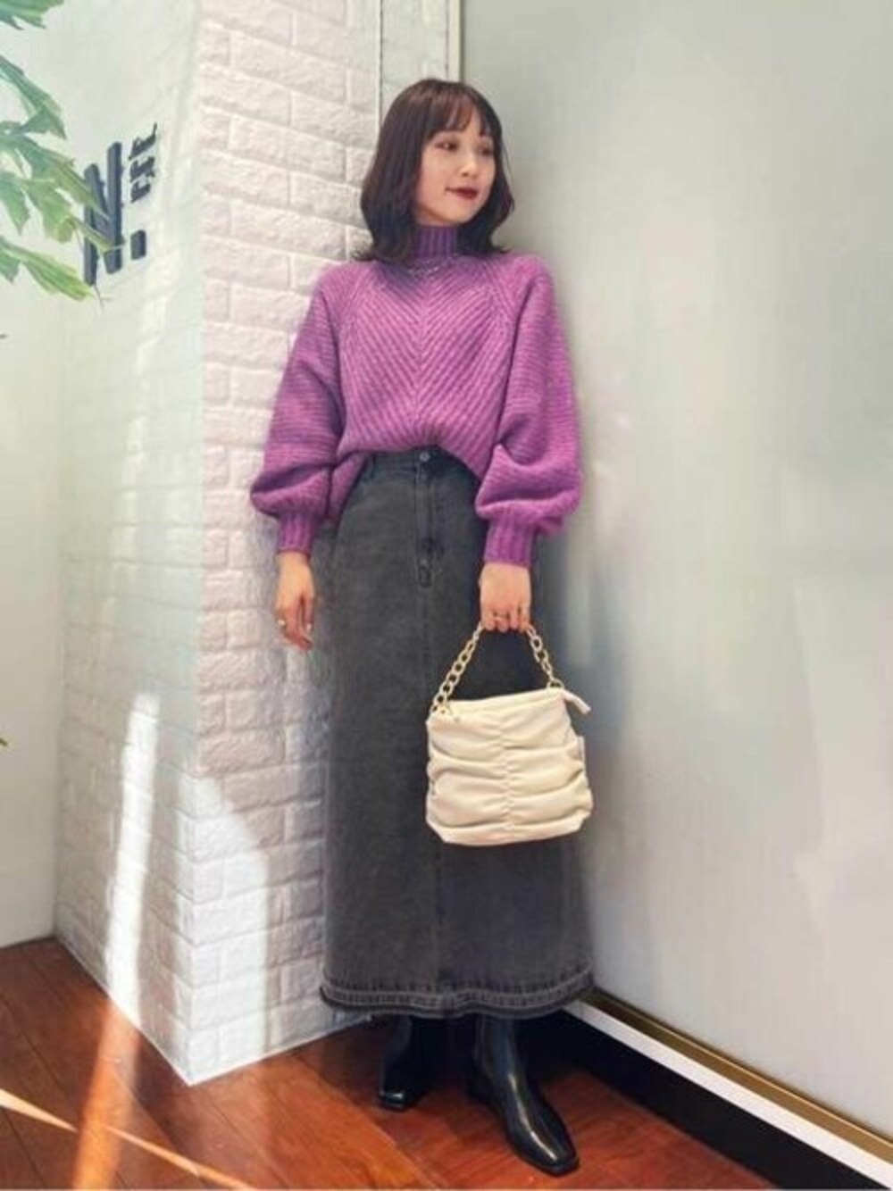 パープル系のニット/セーター、グレー系のデニムスカート、ブラック系のブーツを着用したレディースの冬コーディネートの1枚目の写真