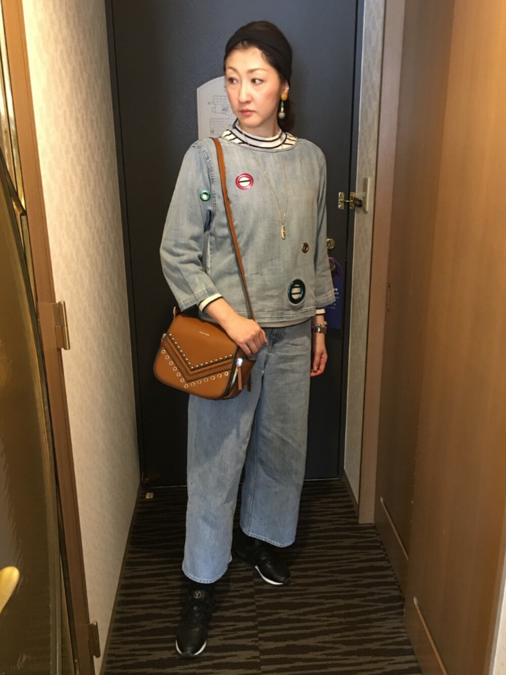 ブルー系のデニムパンツ、ブラウン系のショルダーバッグ、ブラック系のスニーカーを着用したレディースの春コーディネートの1枚目の写真