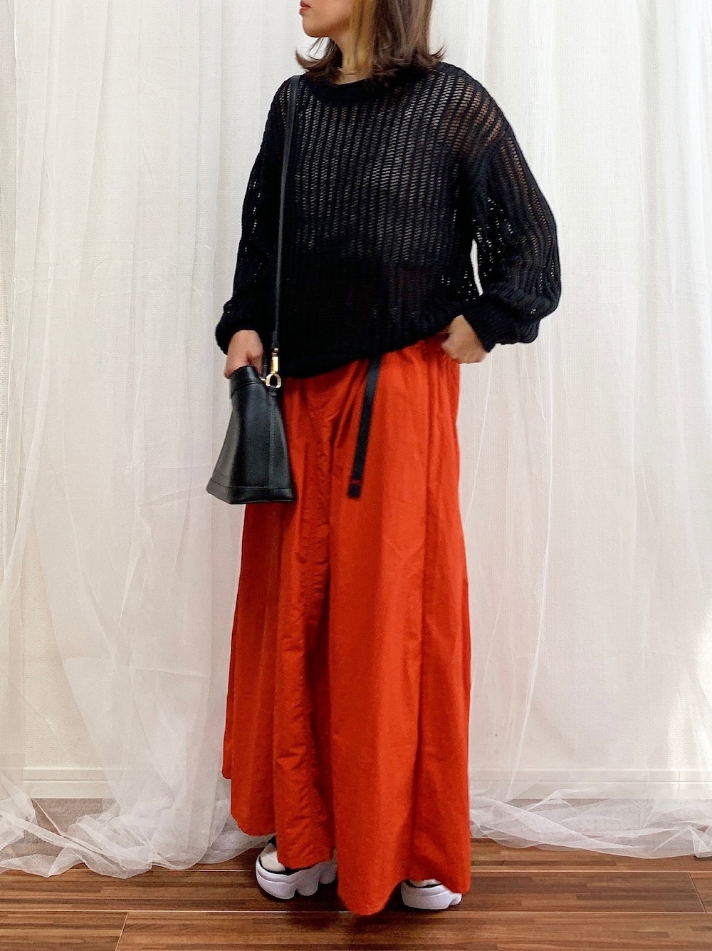 ブラック系のニット/セーター、オレンジ系のスカート、ブラック系のショルダーバッグを着用したレディースの春コーディネートの1枚目の写真