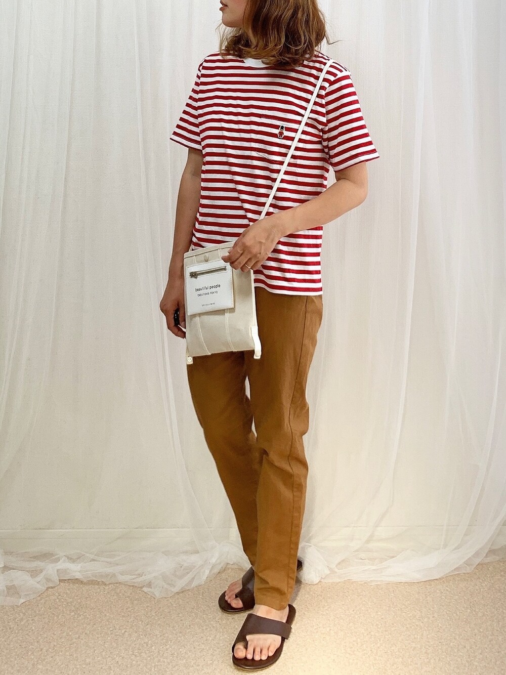 レッド系のTシャツ/カットソー、ホワイト系のショルダーバッグ、ブラウン系のチノパンツを着用したレディースの夏コーディネートの1枚目の写真