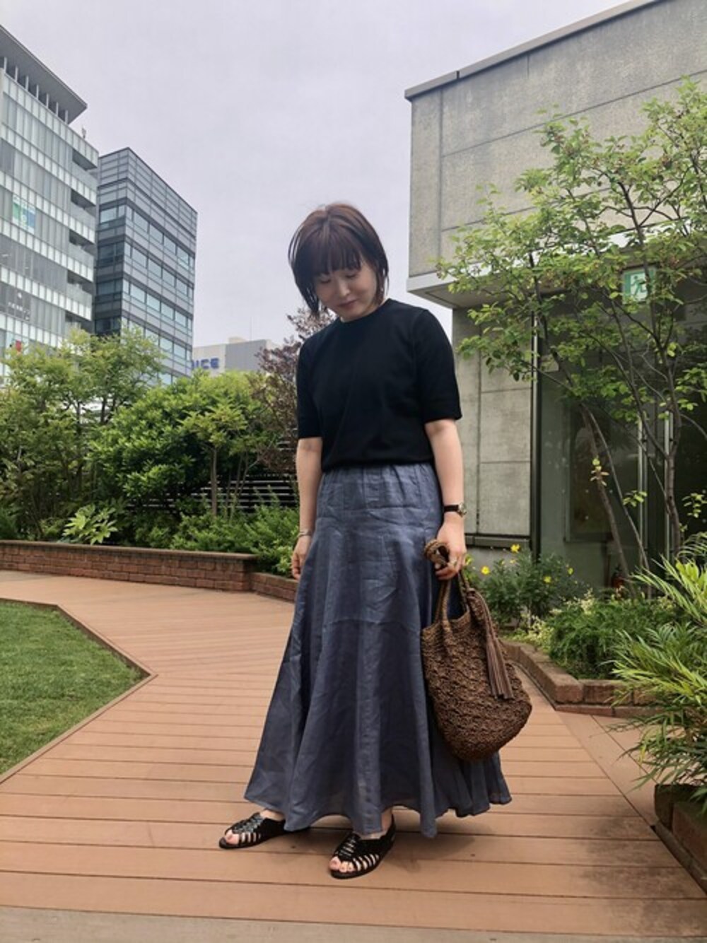 ブラック系のニット/セーター、ブルー系のスカート、ブラウン系のショルダーバッグを着用したレディースの春コーディネートの1枚目の写真