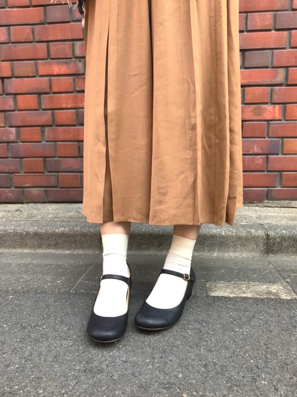 ブラウン系のスカート、ブラック系のパンプスを着用したレディースの冬コーディネートの1枚目の写真