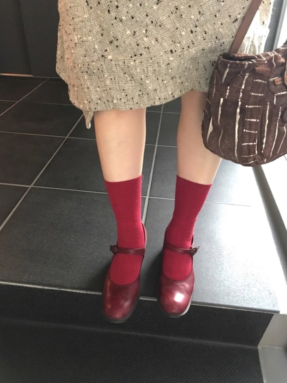 レッド系のパンプス、ベージュ系のスカート、ブラウン系のハンドバッグを着用したレディースの冬コーディネートの1枚目の写真