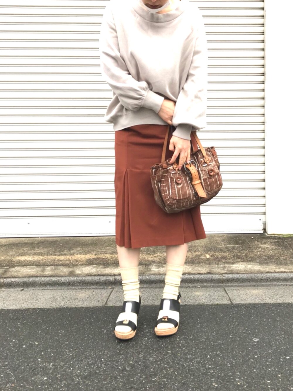 ベージュ系のスウェット、ブラウン系のスカート、ブラウン系のハンドバッグを着用したレディースの春コーディネートの1枚目の写真