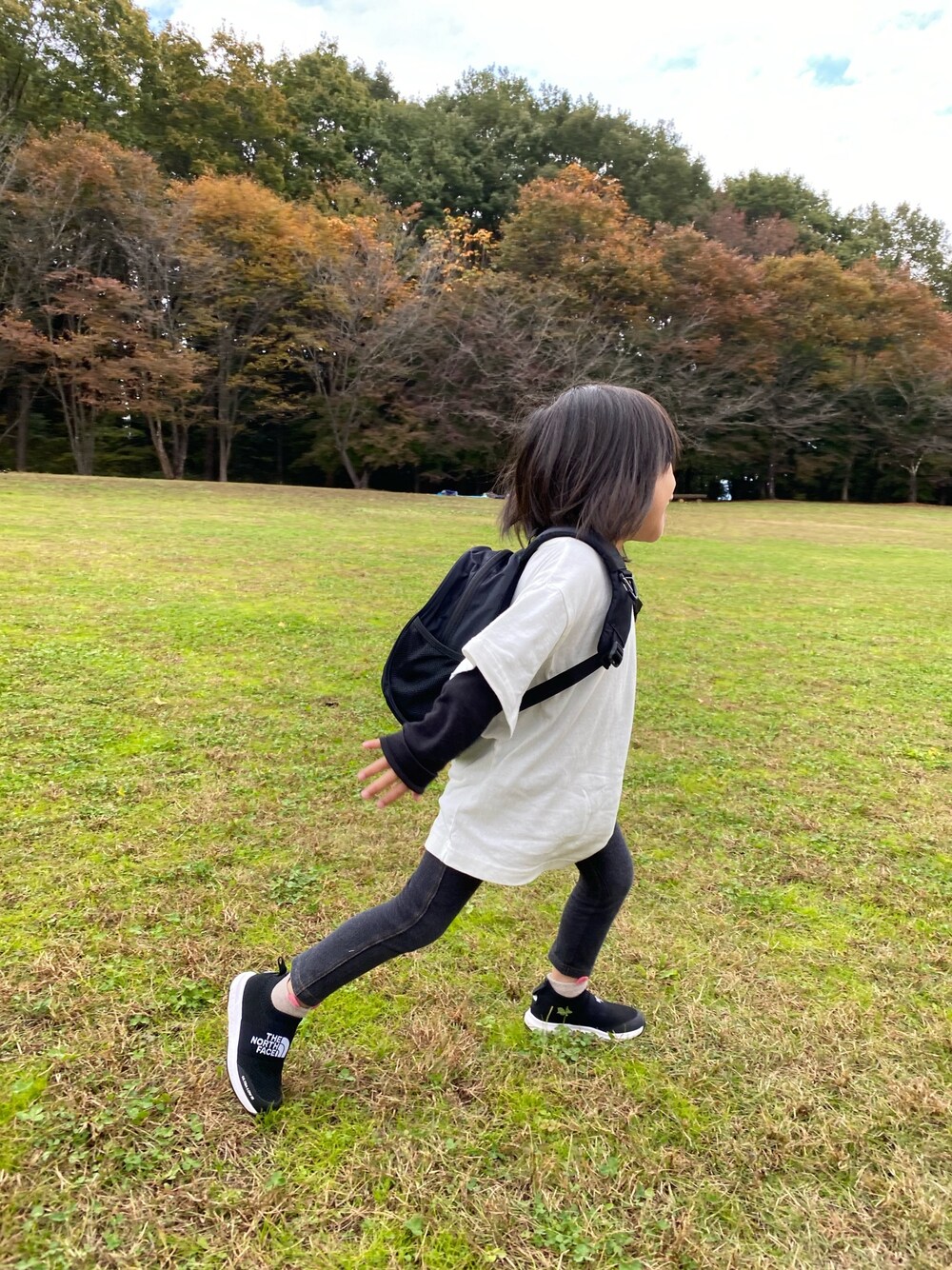 ブラック系のバックパック/リュック、ホワイト系のTシャツ/カットソー、ブラック系のスニーカーを着用したキッズの秋コーディネートの1枚目の写真