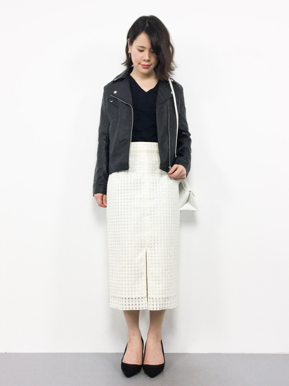 ブラック系のライダースジャケット、ブラック系のニット/セーター、ホワイト系のスカートを着用したレディースの春コーディネートの1枚目の写真