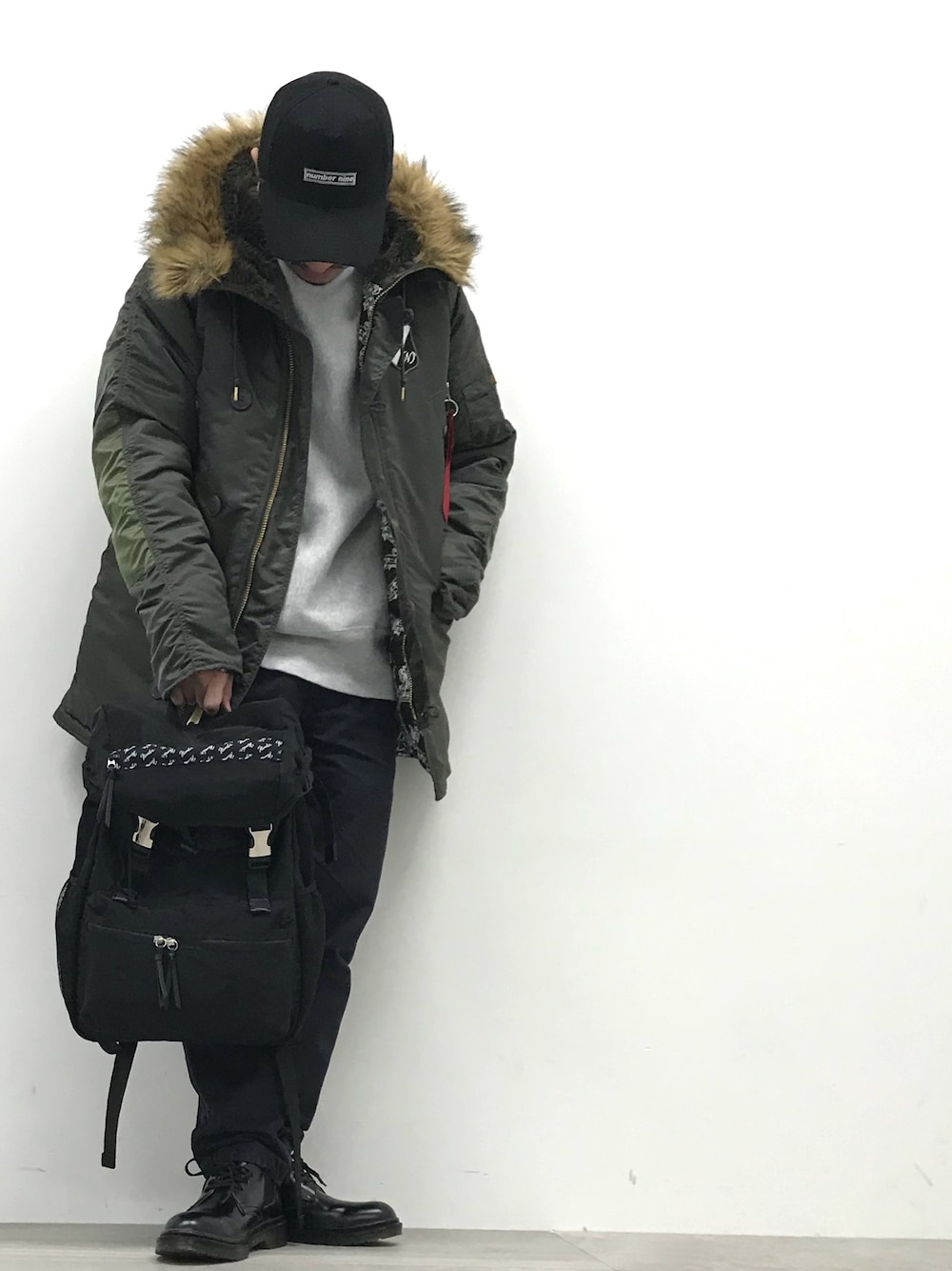 グリーン系のミリタリージャケット、ブラック系のバックパック/リュック、ブラック系のドレスシューズを着用したメンズの冬コーディネートの1枚目の写真