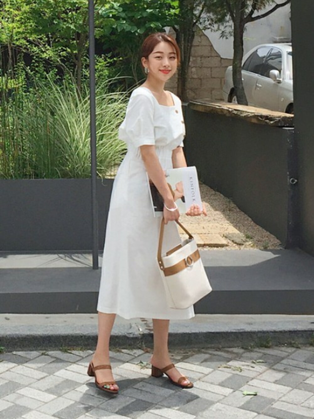 ホワイト系のワンピース、ブラウン系のトートバッグ、ブラウン系のサンダルを着用したレディースの夏コーディネートの1枚目の写真