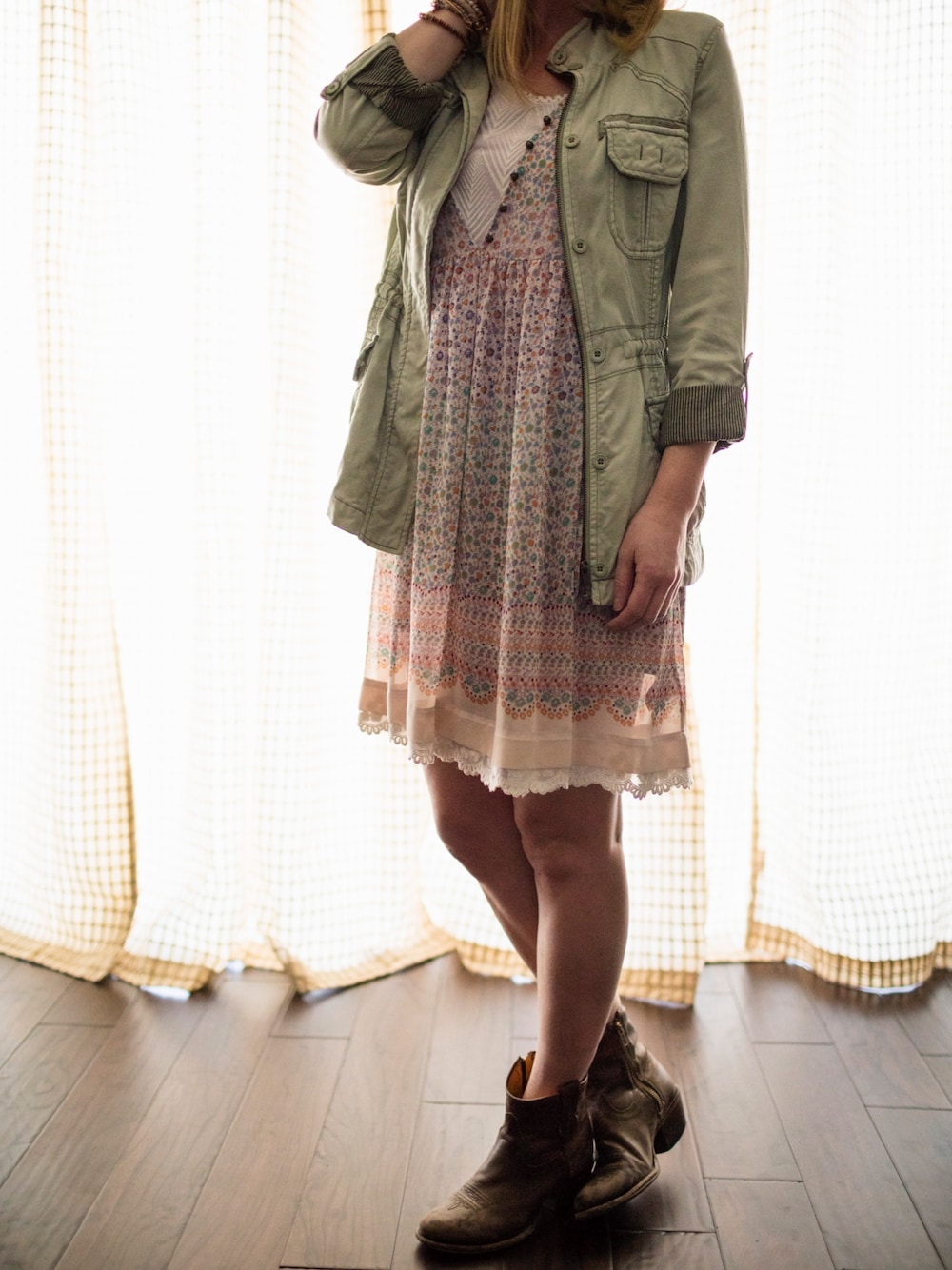 グレー系のドレス、グリーン系のミリタリージャケット、ブラウン系のブーティを着用したレディースの春コーディネートの1枚目の写真