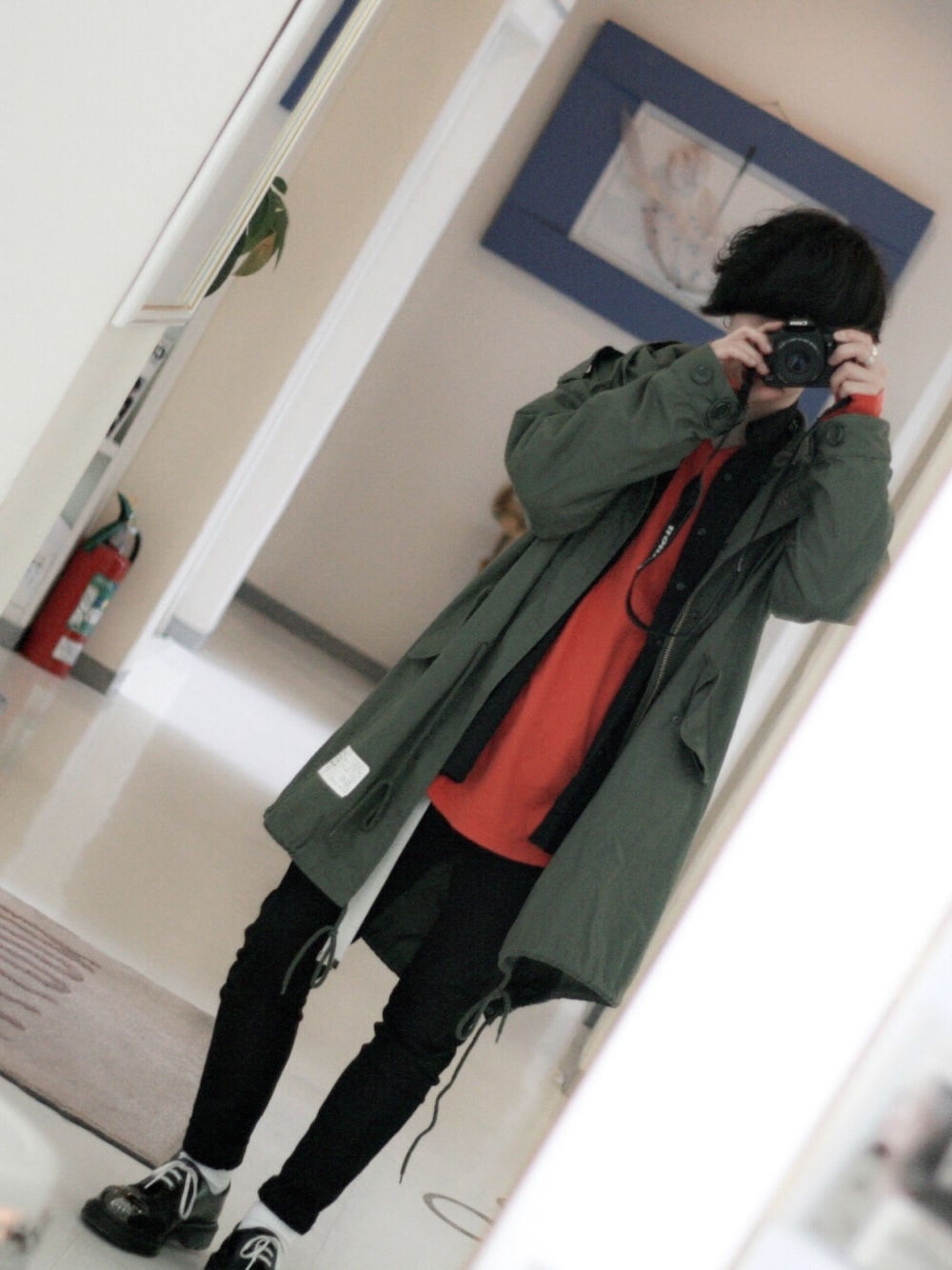 グリーン系のモッズコート、ブラック系のシャツ/ブラウス、オレンジ系のTシャツ/カットソーを着用したメンズの冬コーディネートの1枚目の写真