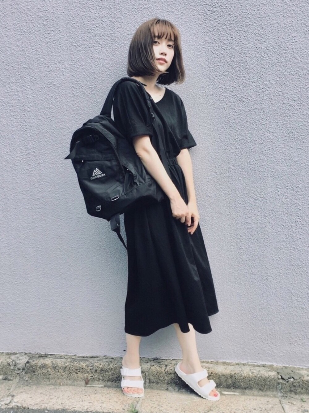 ブラック系のワンピース、ブラック系のバックパック/リュック、ホワイト系のサンダルを着用したレディースの夏コーディネートの1枚目の写真