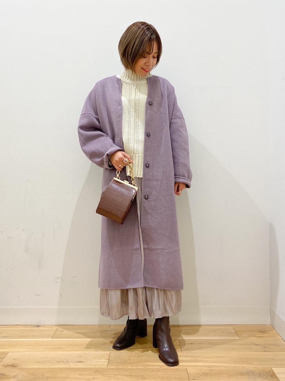 パープル系のノーカラージャケット、ホワイト系のニット/セーター、ブラウン系のショルダーバッグを着用したレディースの冬コーディネートの1枚目の写真