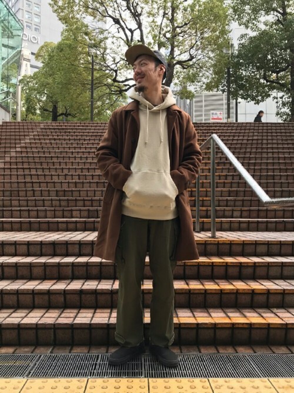 ブラウン系のステンカラーコート、ベージュ系のパーカーを着用したメンズの冬コーディネートの1枚目の写真