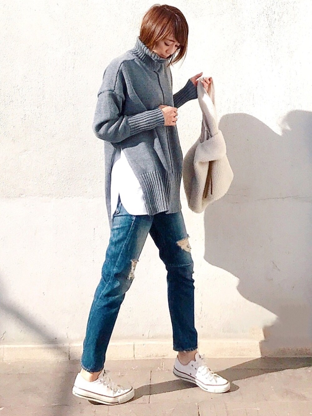 グレー系のニット/セーター、ホワイト系のタンクトップ、ブルー系のデニムパンツを着用したレディースの秋コーディネートの1枚目の写真