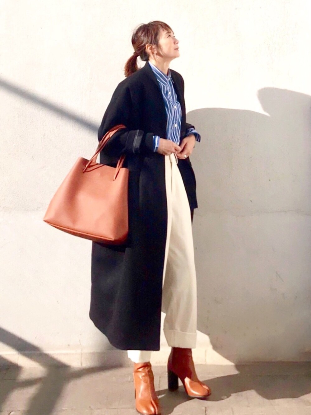 イエロー系のブーツ、ブラウン系のトートバッグ、ブラック系のノーカラーコートを着用したレディースの冬コーディネートの1枚目の写真