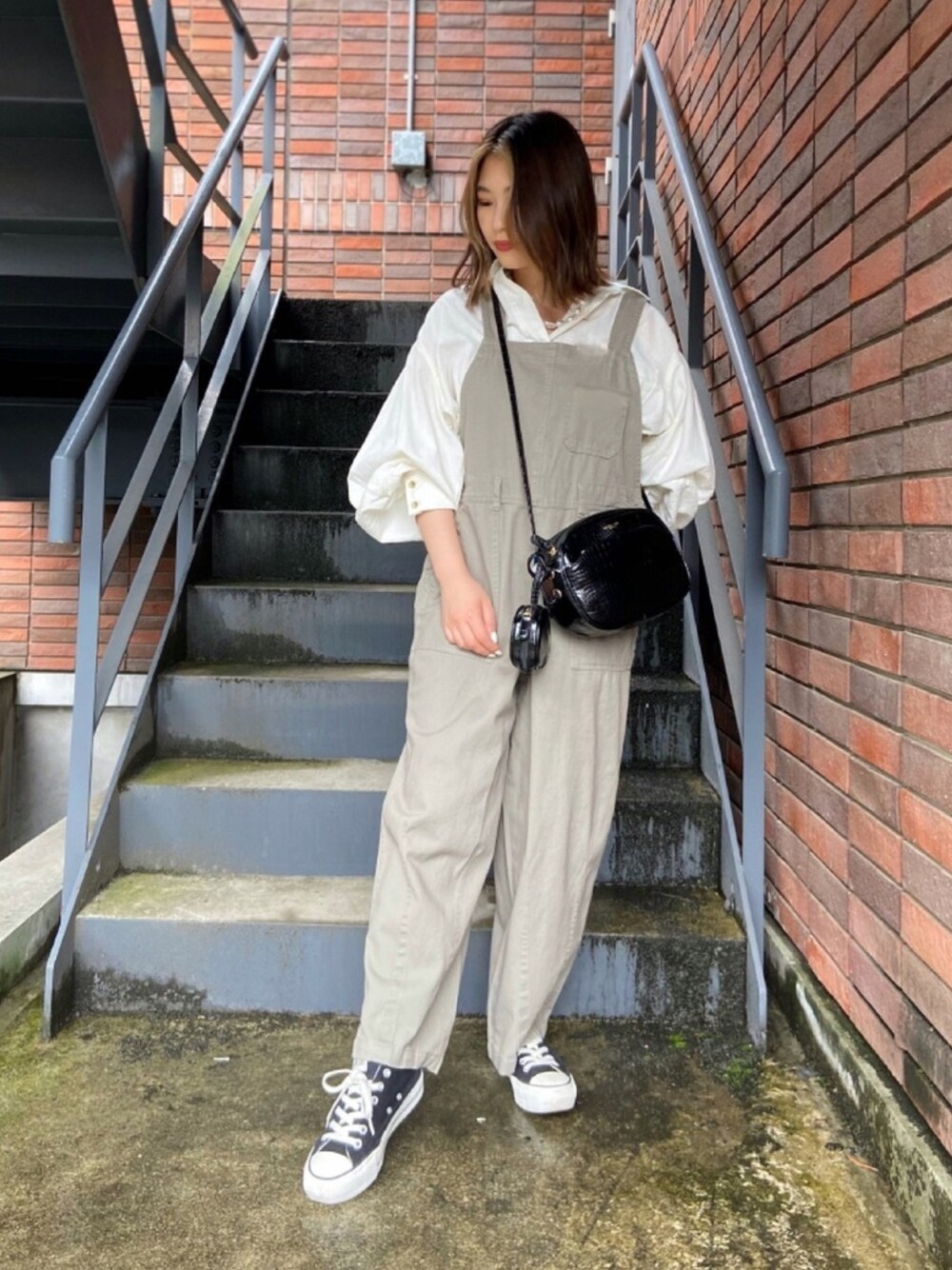 ホワイト系のシャツ/ブラウス、グレー系のサロペット/オーバーオール、ブラック系のショルダーバッグを着用したレディースの春コーディネートの1枚目の写真
