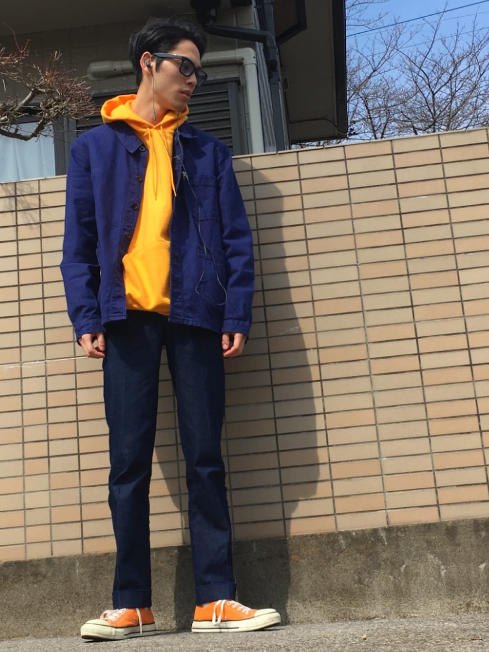 イエロー系のパーカー、ブルー系のカバーオール、ブルー系のスラックスを着用したメンズの春コーディネートの1枚目の写真