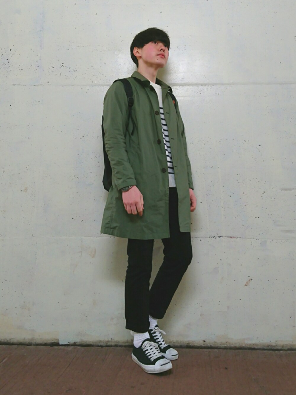 グリーン系のステンカラーコート、ホワイト系のニット/セーター、ブラック系のバックパック/リュックを着用したメンズの春コーディネートの1枚目の写真